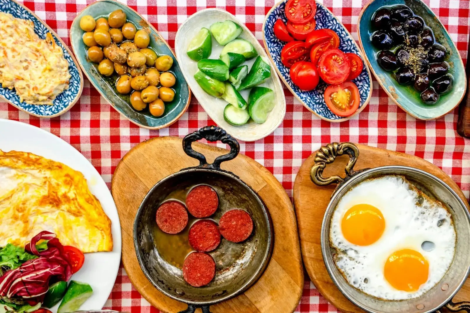Turkish breakfast table with olives, cucumbers, tomatoes, sucuk and fried eggs